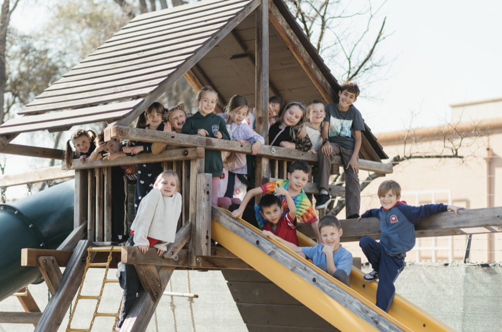 Legacy students gathered on the playground fort and slide, smiling at the camera